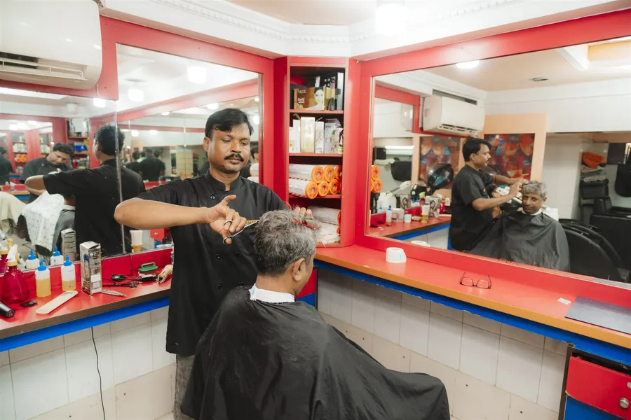 A barber cutting an older customer’s grey hair with scissors