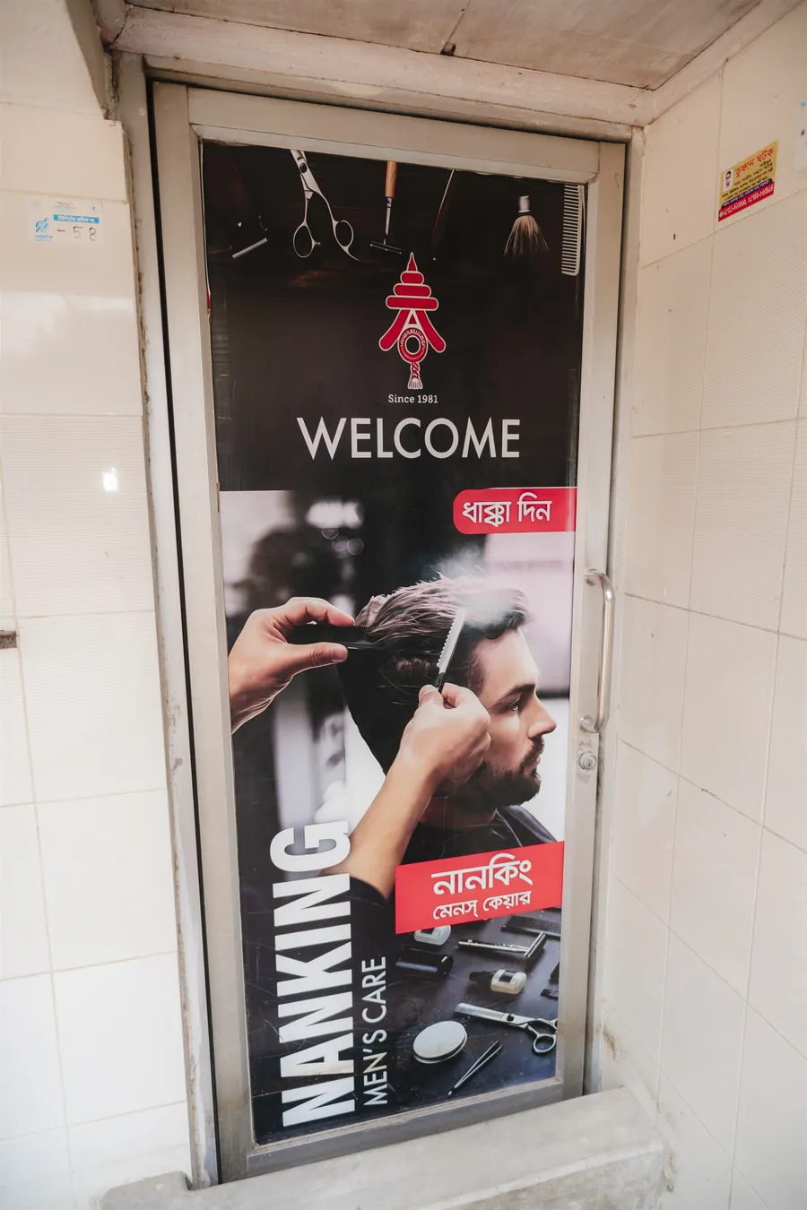 The glass door of Nanking Men’s Care with a Welcome poster and the Nanking logo