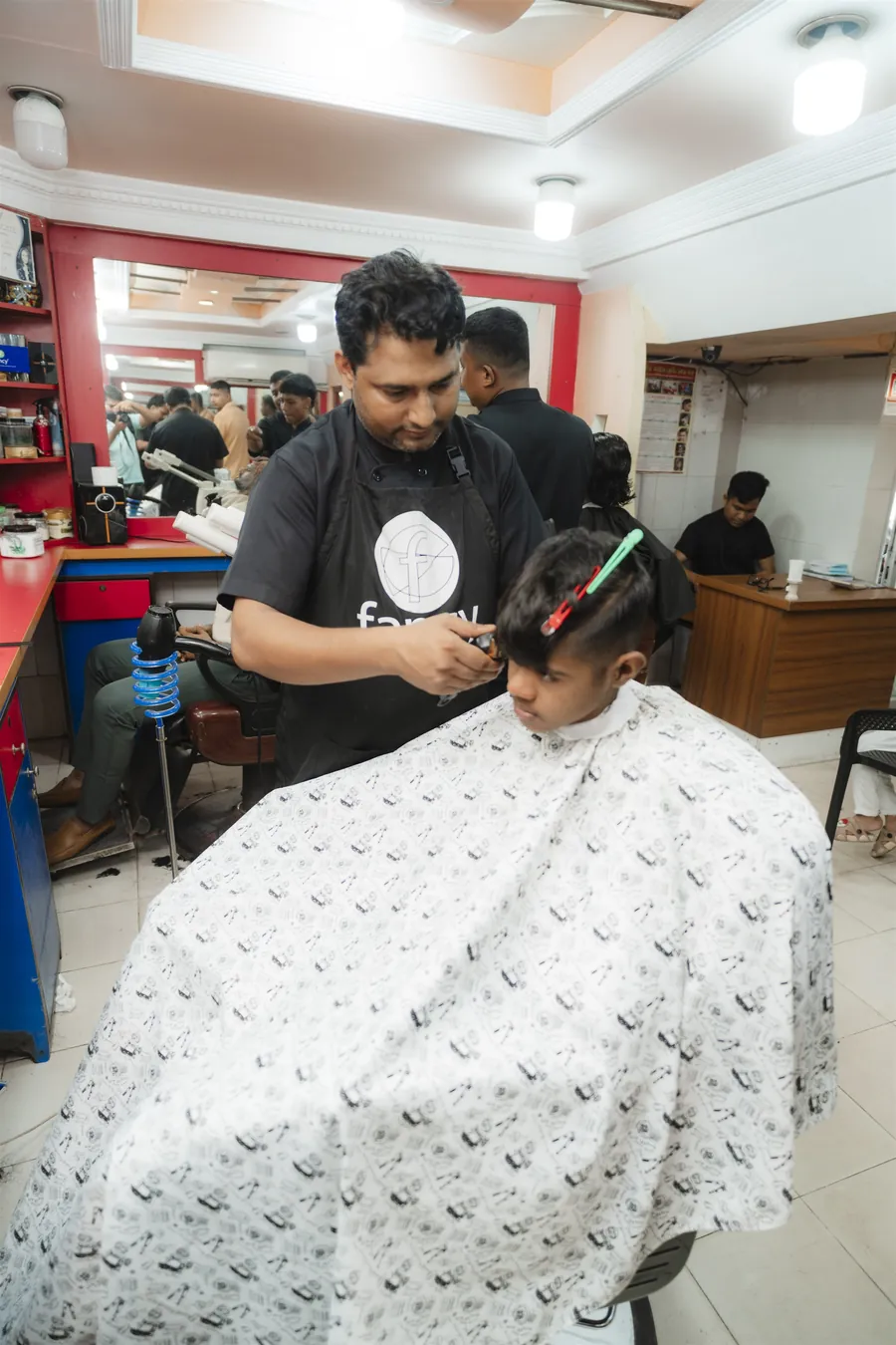 A barber trimming a child’s hair under a printed cape