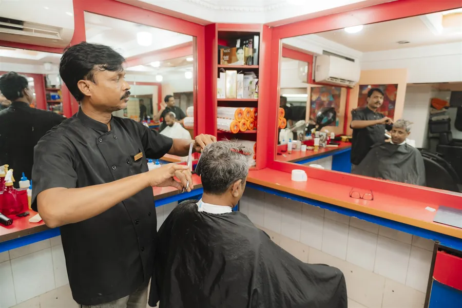 A barber finishing a cut with scissors at the mirror