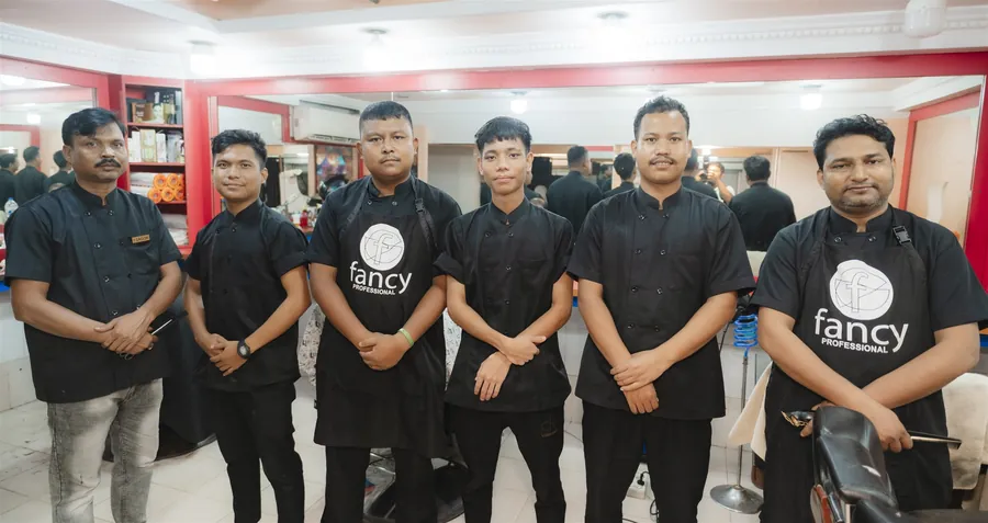 Six barbers of Nanking Men’s Care in black uniforms, standing in a row on the saloon floor