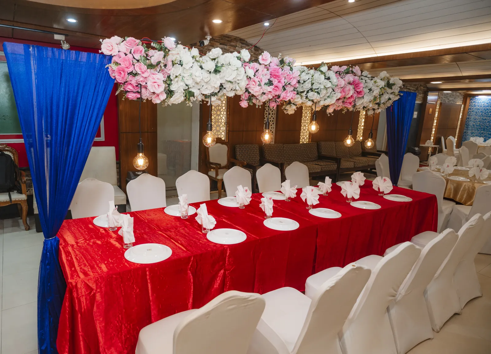 A long table with red cloths and folded white napkins under an arch of pink and white flowers
